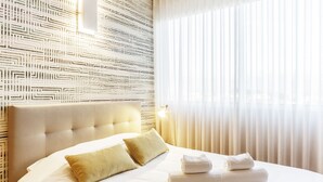 A hotel room with a tufted headboard, a neatly made bed with white linens and two pillows, and a window with sheer curtains. - Praça 66 Guest House (Porto)