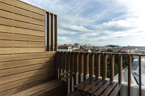 A wooden balcony with a bench, overlooking a cityscape with buildings and a construction crane.