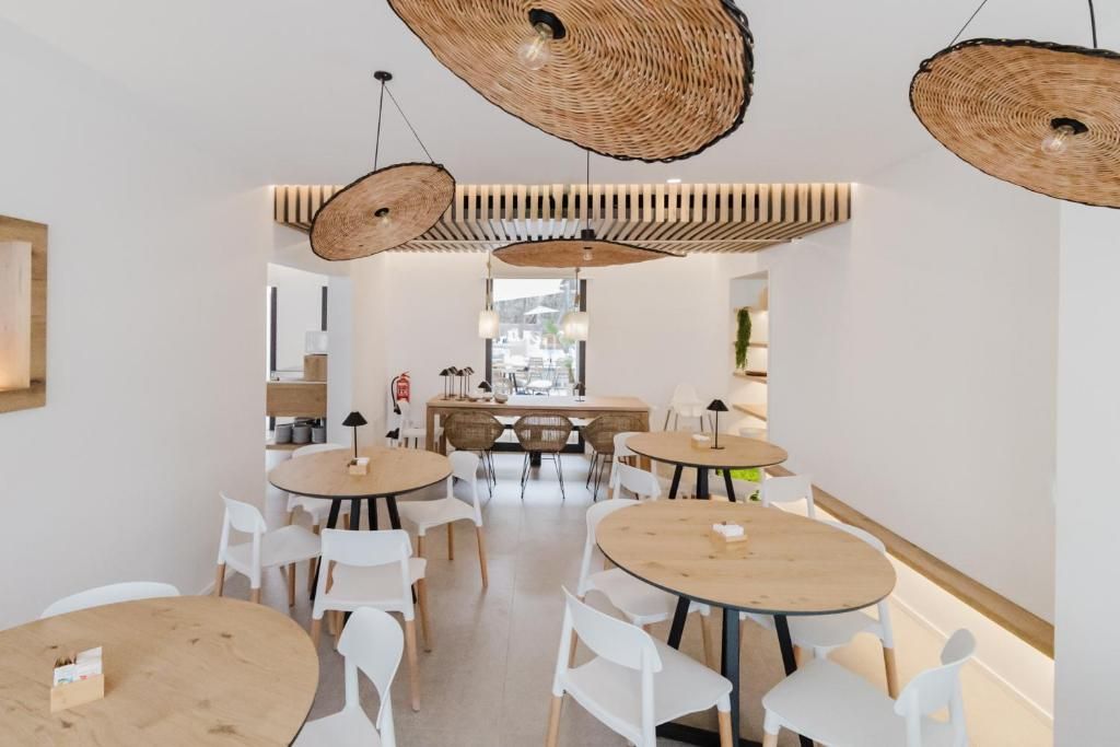 A modern dining area with round tables and white chairs, featuring woven ceiling light fixtures and a view through a glass door.