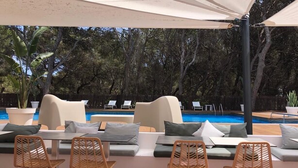 Uma área de estar junto à piscina, com cadeiras de descanso e um toldo.