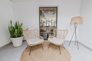 A room with two wicker chairs, a woven rug, a potted plant, and a floor lamp. - Apartamentos Es Pujols (Formentera)