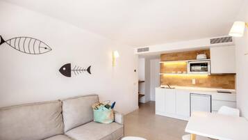 A modern living room with a sofa, a dining table with chairs, a kitchen area with a microwave, and a wall-mounted fish decoration.