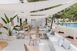 An outdoor seating area with tables and chairs, a pool, and potted plants. - Apartamentos Es Pujols (Formentera)