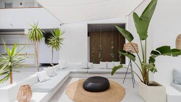 Una sala moderna con un sofá blanco, un otoman negro redondo y diversas plantas.