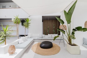 A modern living room with a white sofa, a round black ottoman, and various plants. - Apartamentos Es Pujols (Formentera)