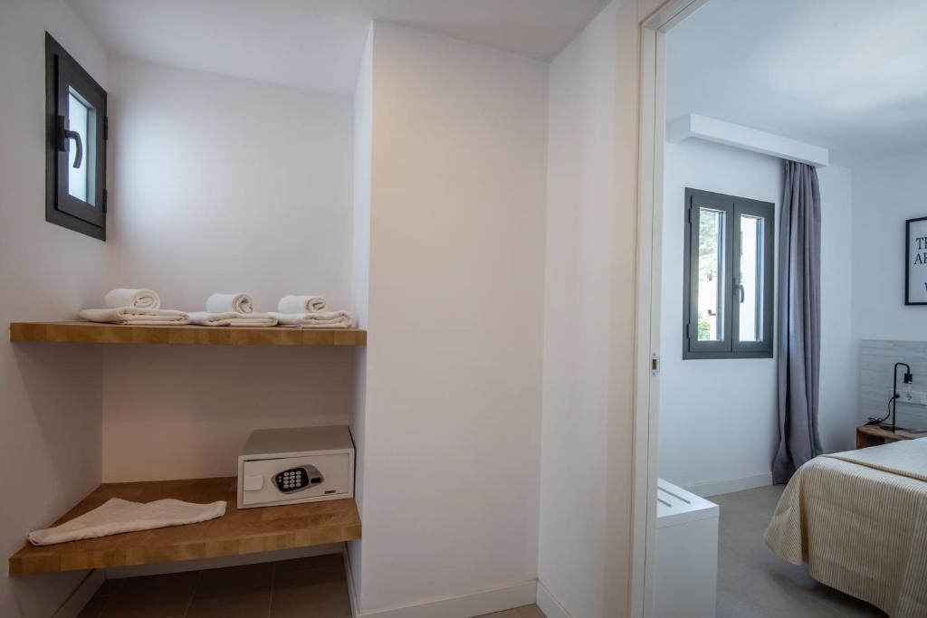 Una habitación de hotel con cama, mesita de noche, estante con toallas y ventana con cortinas.