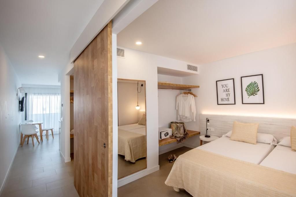 Habitación de hotel con cama, mesita de noche y espejo. Se observa un escritorio con silla y una ventana.