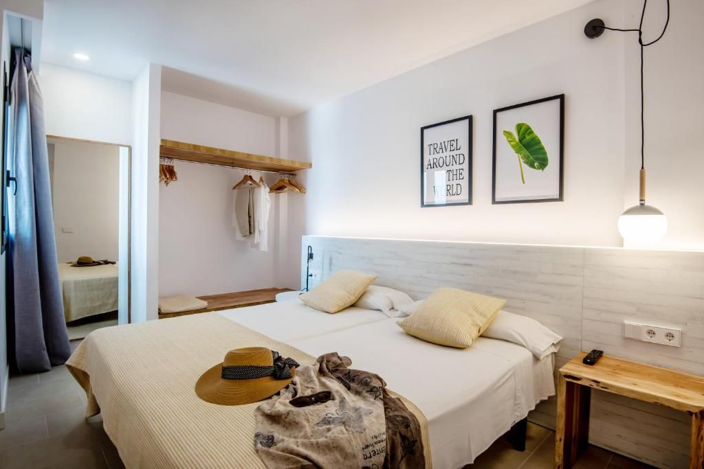 A hotel room with a bed, a bedside table, a hanging light fixture, and a wall-mounted outlet.