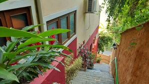 A narrow stone pathway flanked by red walls and potted plants, leading to a building entrance. - Memorial Ilhabela Residencial (Ilhabela)