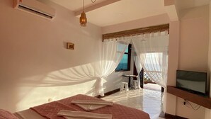 A bedroom with a bed, a TV, and a window with sheer curtains. - Memorial Ilhabela Residencial (Ilhabela)