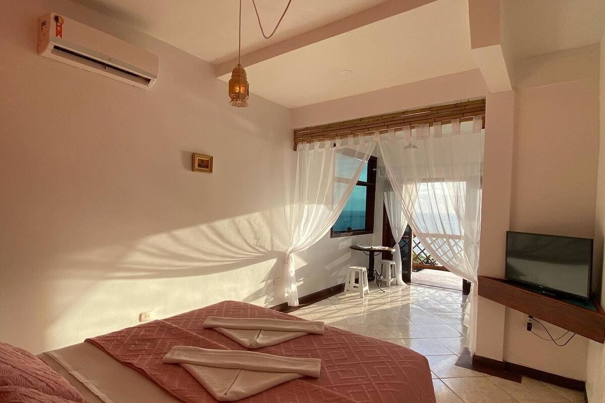 A bedroom with a bed, a TV, and a window with sheer curtains.