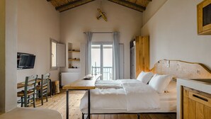 Un dormitorio con cama, escritorio, sillas, televisor y ventana con cortinas.