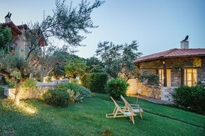 A stone house with a tiled roof, surrounded by a well-maintained garden with a lawn and a wooden chair. - Mazaraki Guesthouse (Sparta)