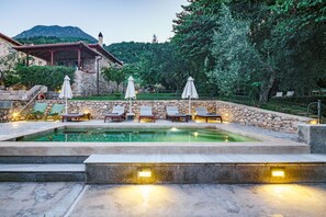 A swimming pool with lounge chairs and umbrellas, surrounded by stone walls and a mountainous backdrop. - Mazaraki Guesthouse (Sparta)