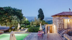 Una villa de piedra con piscina, mobiliario exterior y vistas al paisaje.