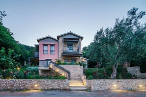 A two-story house with a stone staircase leading to the entrance, surrounded by lush greenery and flowering plants. - Mazaraki Guesthouse (Sparta)