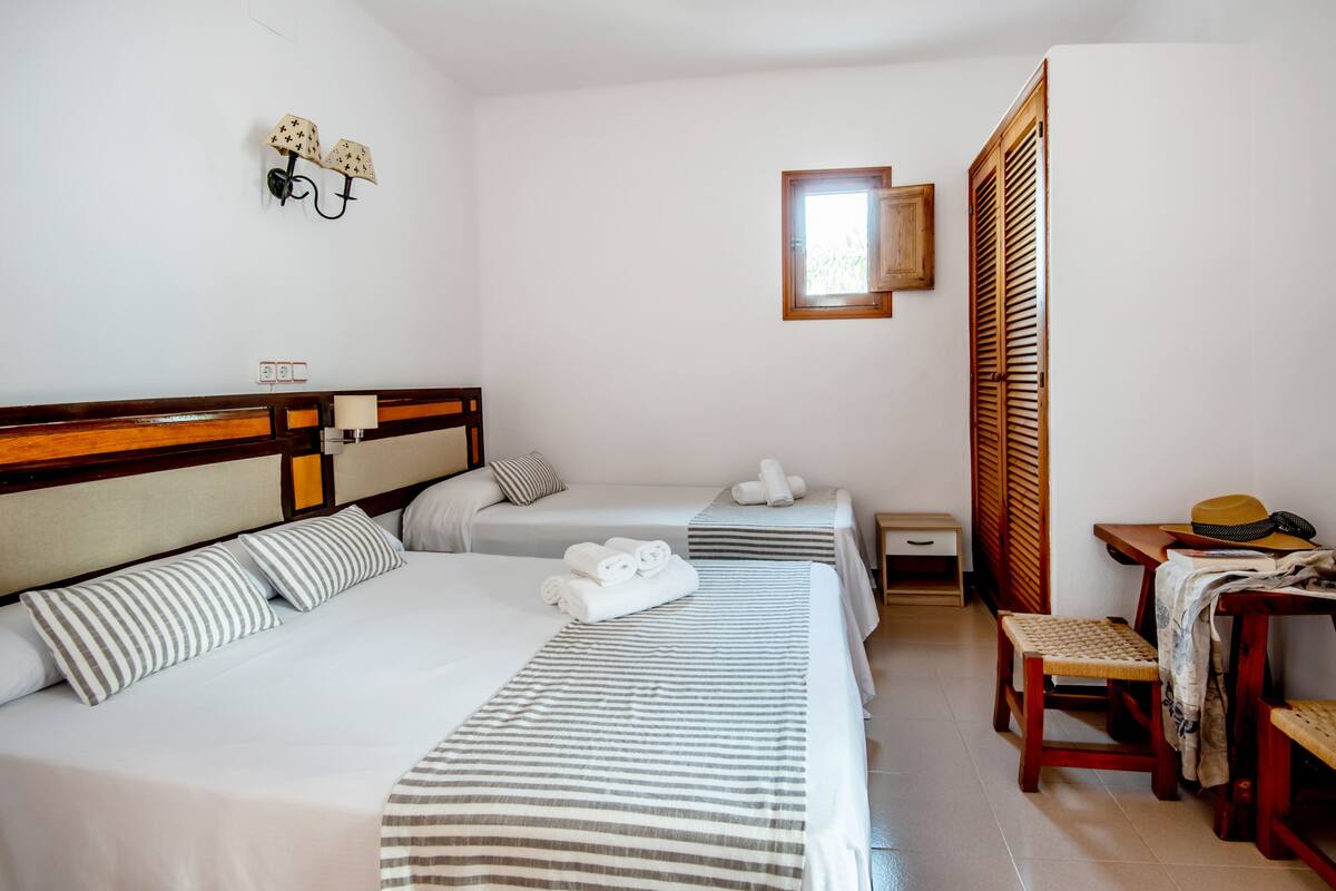 A hotel room with two beds, a wooden headboard, a small table with a hat, and a wooden wardrobe.