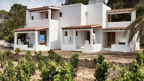 Un edificio moderno blanco de varios niveles y techo de tejas, rodeado de un viñedo.