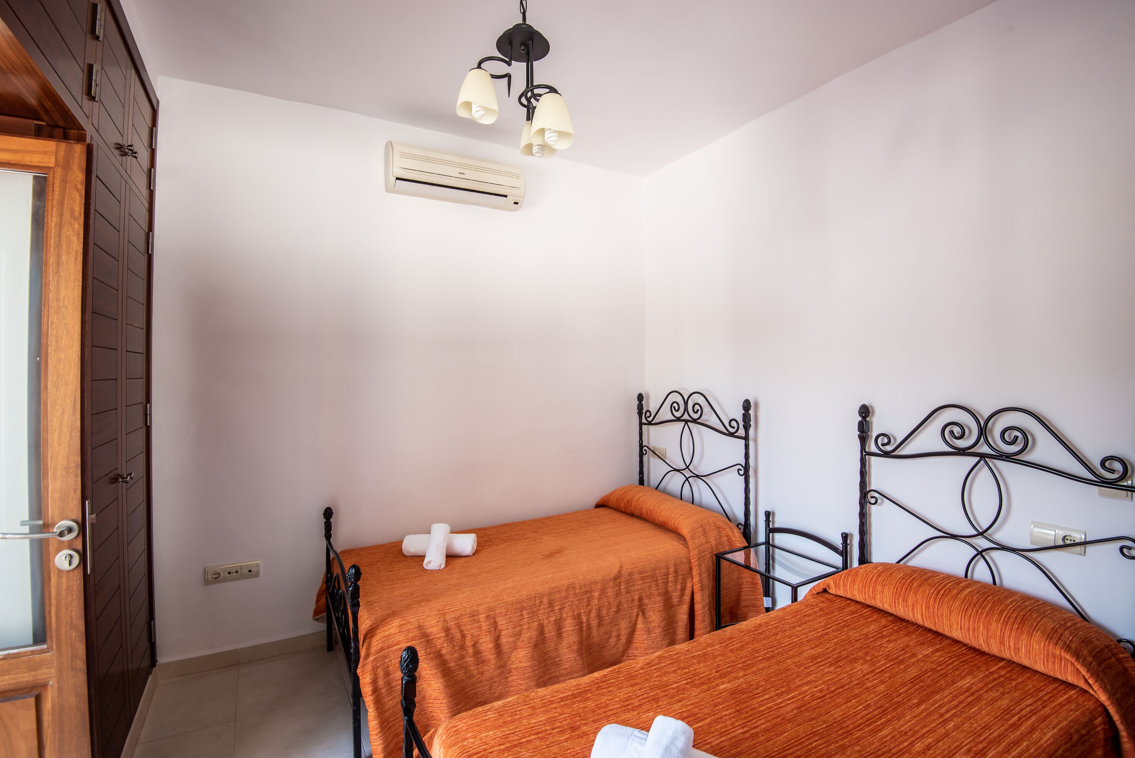 A bedroom with two beds, an air conditioning unit, a ceiling light fixture, and a wooden door.