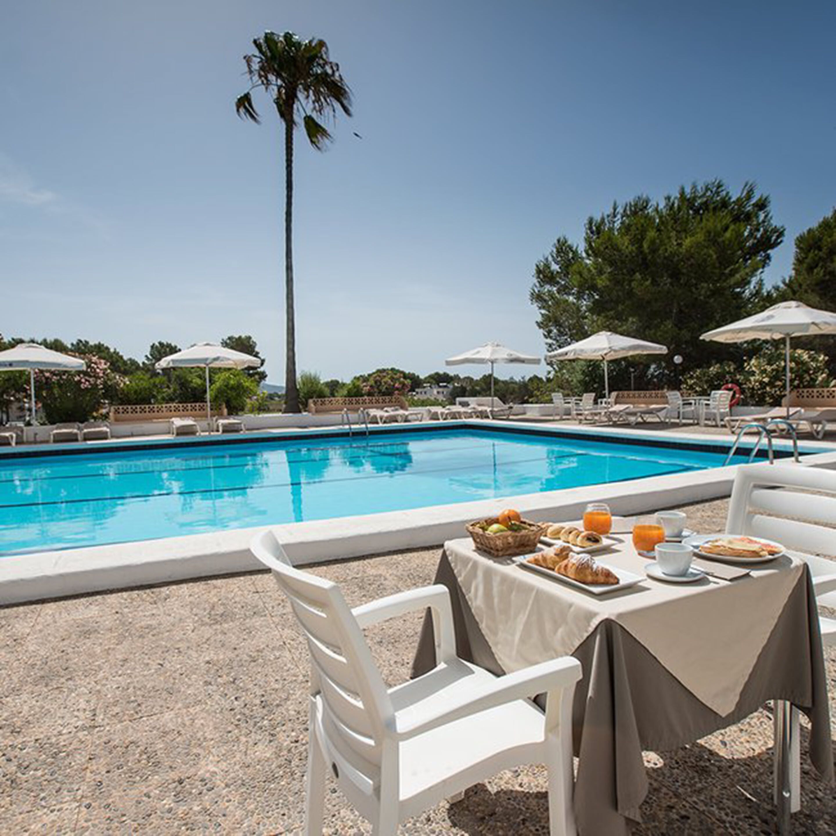 A poolside dining area with a table set for breakfast, surrounded by lounge chairs and umbrellas.