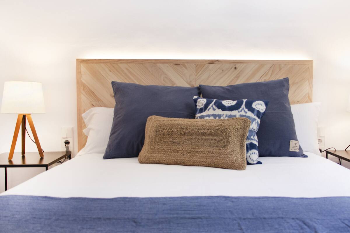 A neatly made bed with a wooden headboard, two bedside tables with lamps, and a variety of pillows.