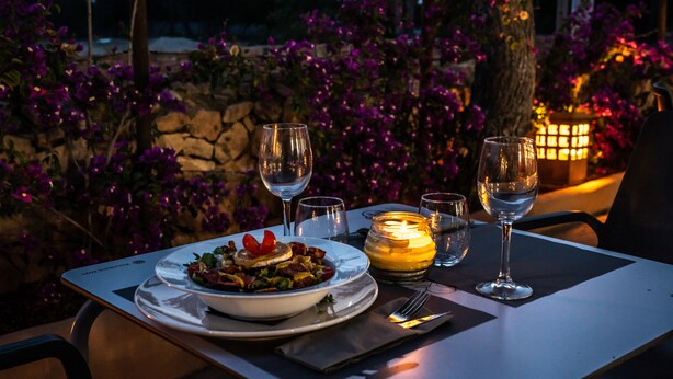 Una mesa lista para la cena, con una vela, copas de vino y un plato de comida.