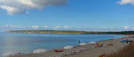 A beach with sun loungers, umbrellas, and a clear sky.