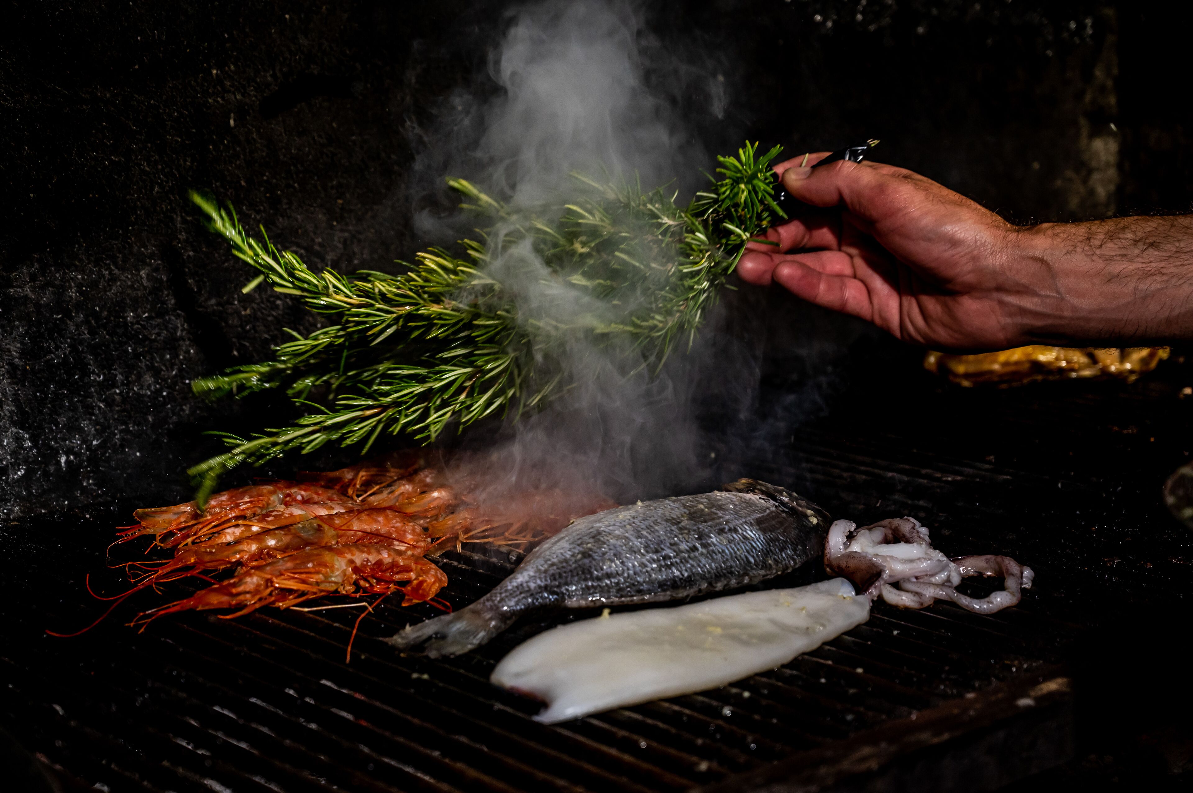 A grill with seafood and a sprig of rosemary.