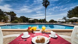 Desayuno junto a la piscina, con una mesa, sillas y una piscina al fondo.
