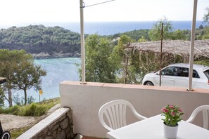 Un balcon avec une table et des chaises blanches, une plante en pot et une vue sur la mer et les collines boisées.