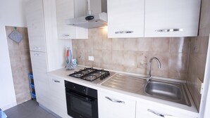 Een moderne keuken met witte kastjes, een roestvrijstalen spoelbak, een gasfornuis en een zwarte oven.