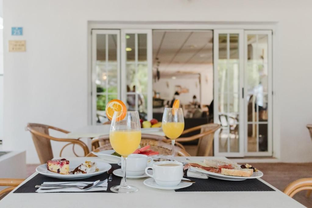 A dining table with plates of food, glasses of orange juice, and a white cup, likely in a restaurant or cafe setting.