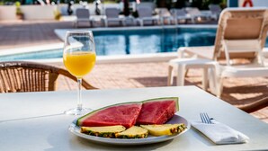 A table with a glass of orange juice, a plate with watermelon and pineapple slices, and a napkin with a fork. - Hostal Es Pi (Formentera)