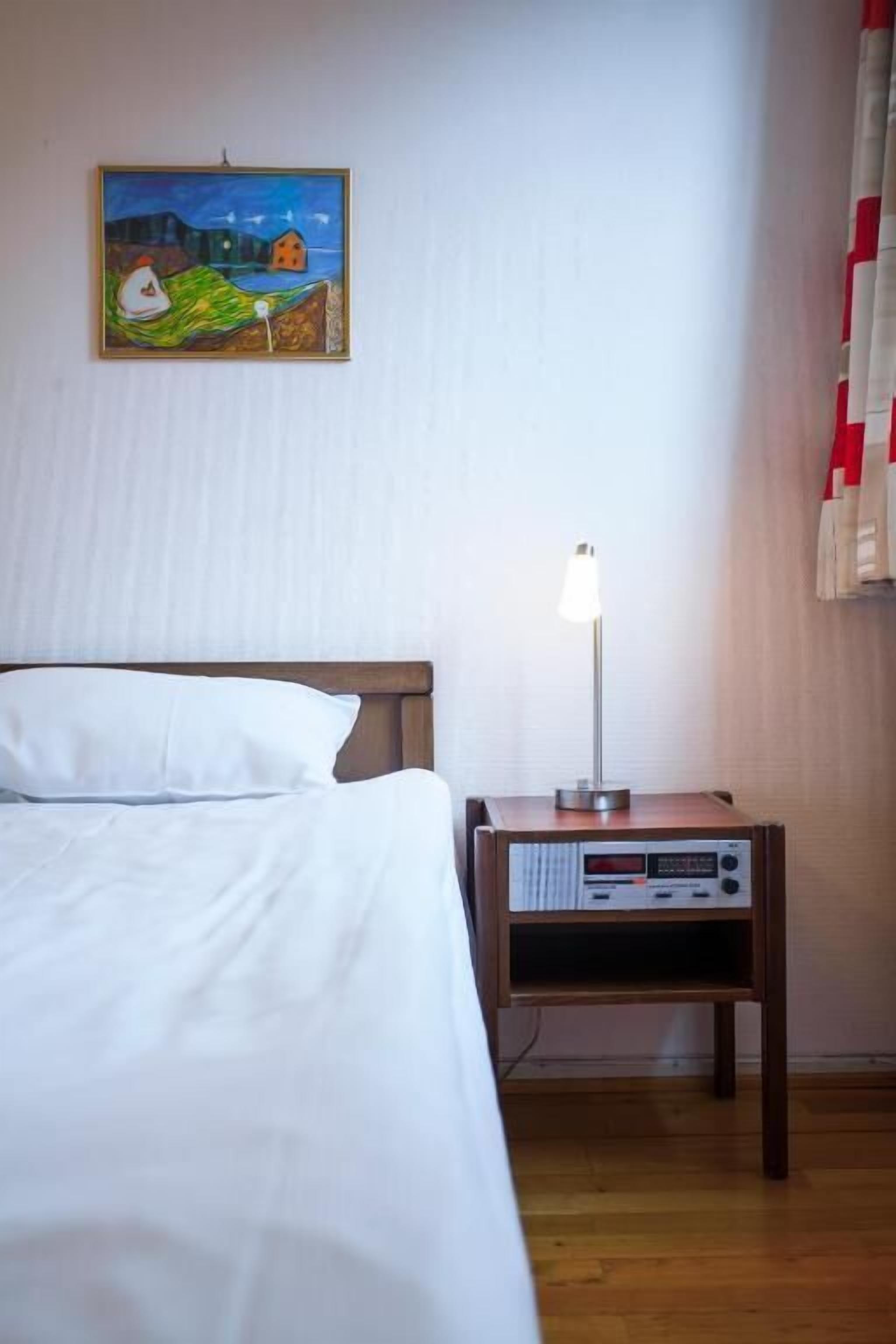 A hotel room with a bed, a nightstand with a lamp, and a painting on the wall.