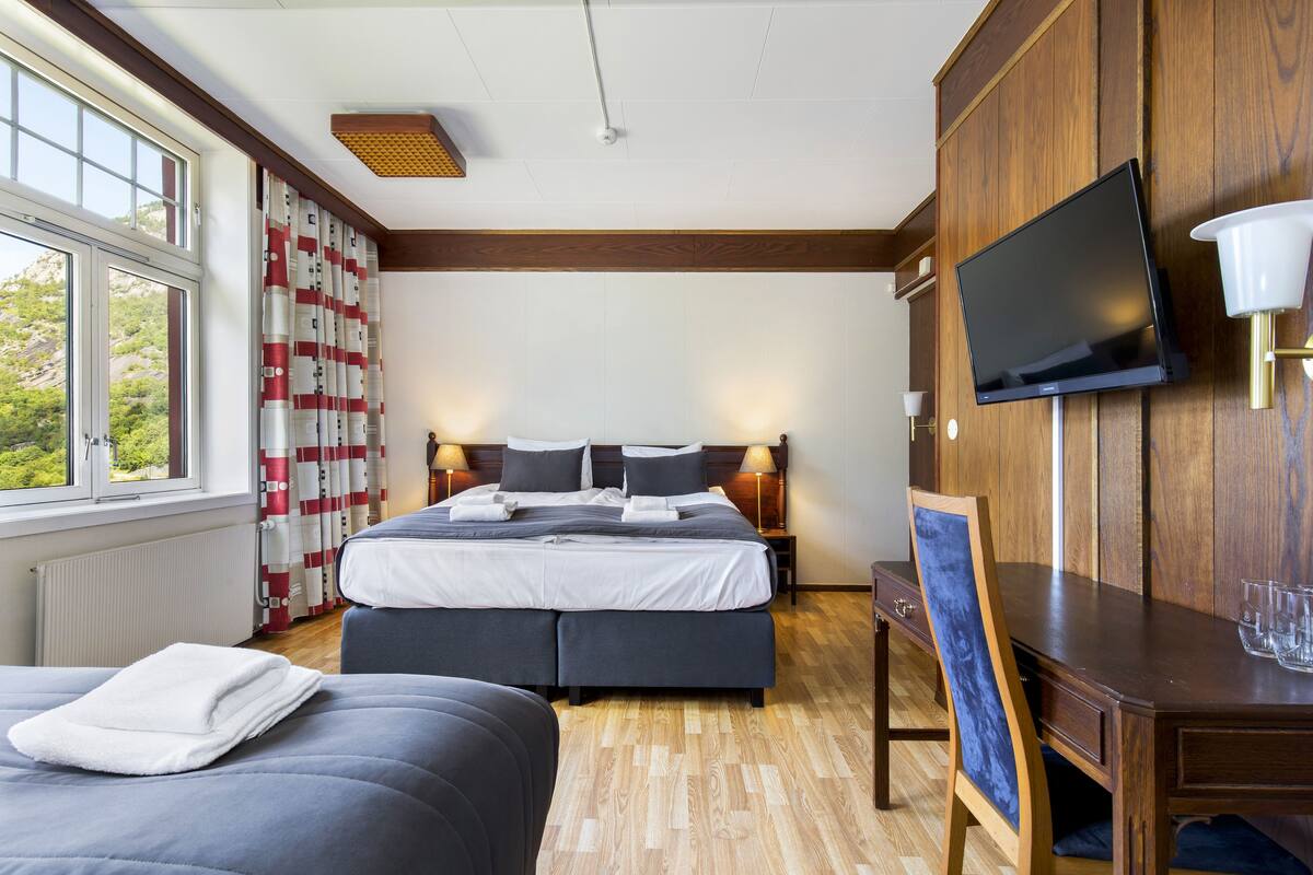 Une chambre à coucher avec un lit, des tables de chevet, une télévision et une fenêtre avec des rideaux.