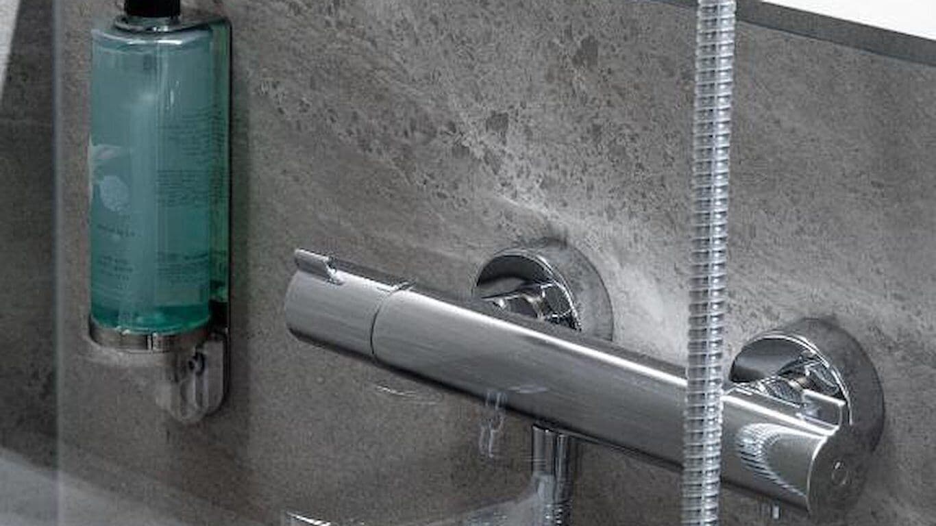 A bathroom with a shower, a faucet, and a soap dispenser.