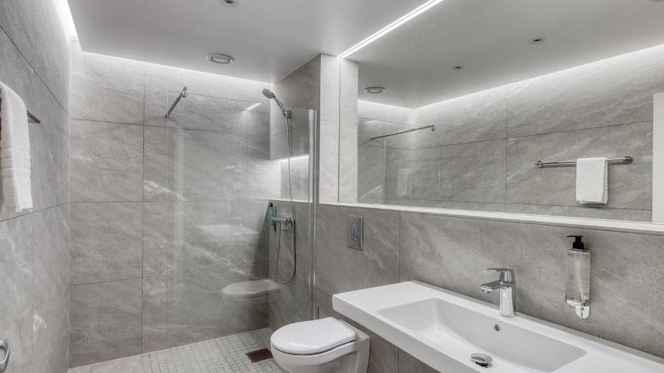Une salle de bain moderne avec une douche à parois de verre, des toilettes blanches et un grand lavabo avec un miroir.