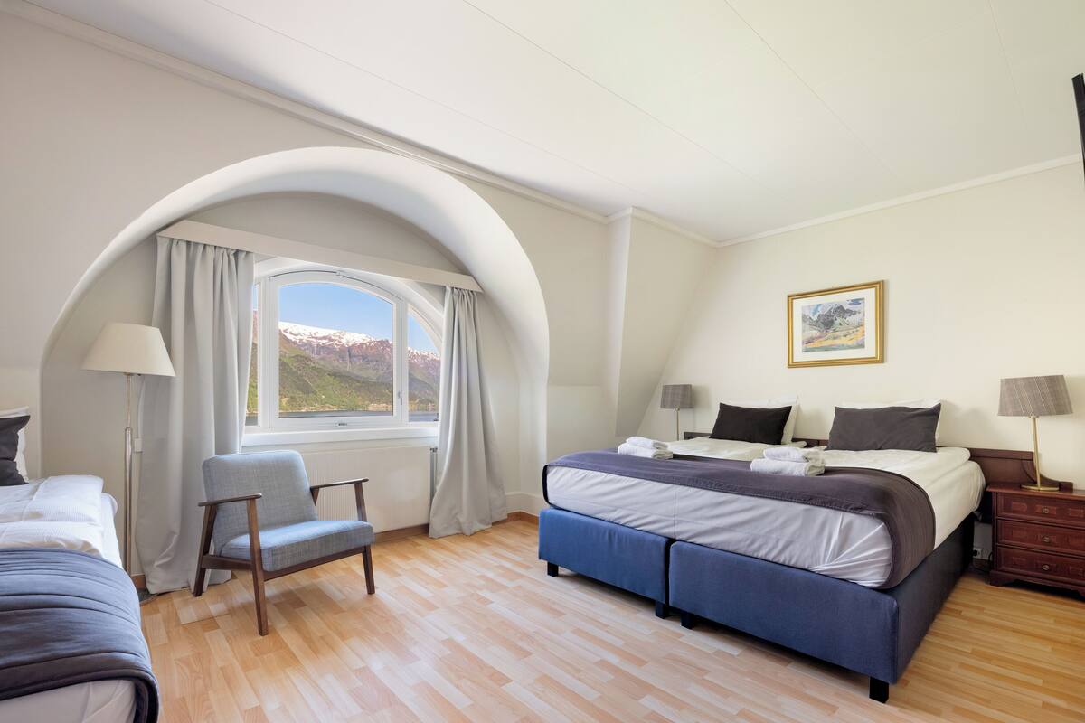 Une chambre avec un grand lit, une chaise, un bureau et une fenêtre donnant sur les montagnes.