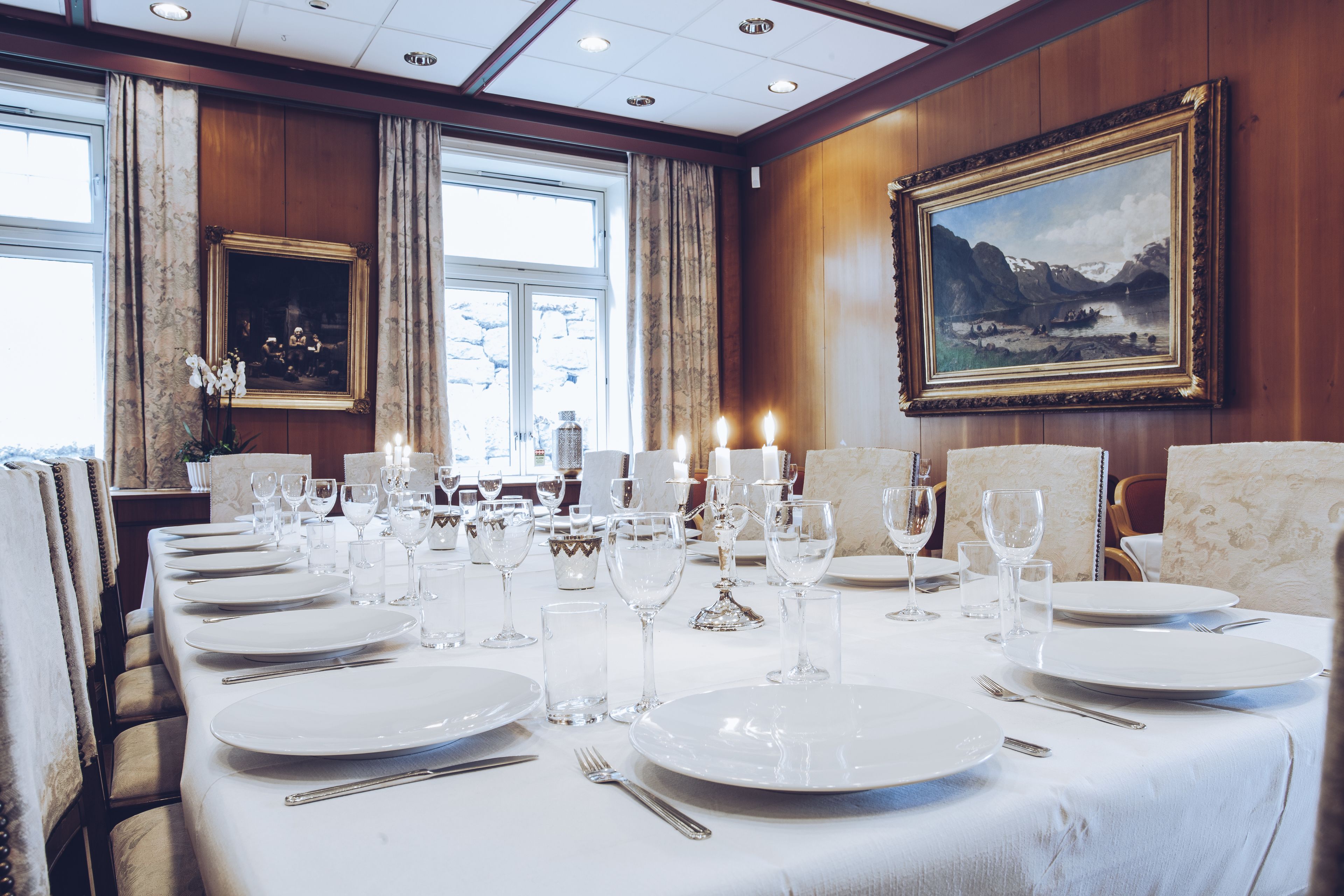 Un comedor formal con una larga mesa dispuesta para una comida, obras de arte enmarcadas en las paredes y amplios ventanales.