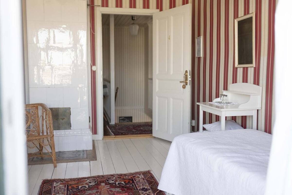A room with a bed, a bedside table, a chair, a door leading to a bathroom, and striped wallpaper.