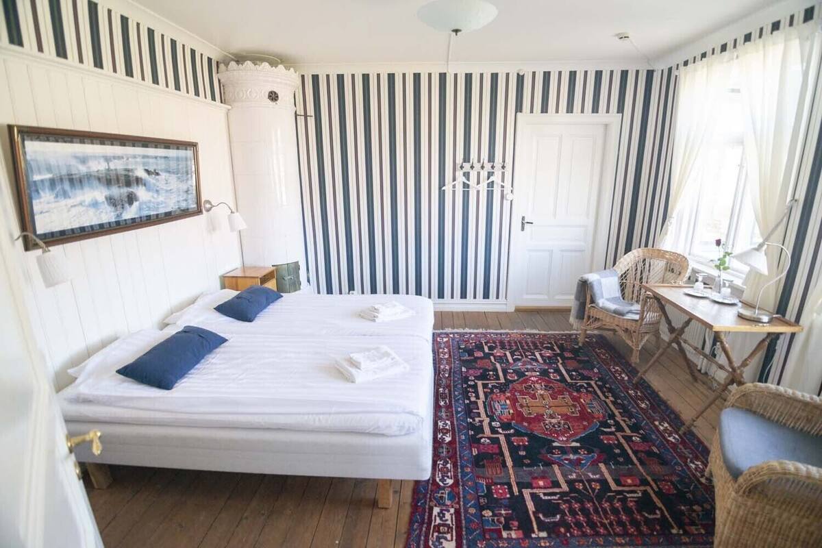 A room with two beds, a desk, a chair, a hanging light fixture, and a striped wall.