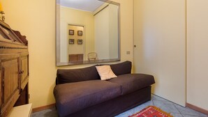 A room with a large mirror, a brown sofa, a wooden cabinet, and a patterned rug. - Impero House Rent - Il Bosco (Stresa)