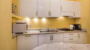 A compact kitchen with white cabinets, a built-in microwave, a gas stove, and a sink. - Impero House Rent - Il Bosco (Stresa)