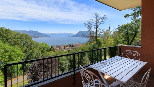 A balcony with a wooden table and chairs, overlooking a scenic view of a lake and mountains. - Impero House Rent - Il Bosco (Stresa)