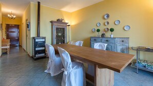 A dining area with a wooden table and chairs, a vintage stove, and a wall decorated with plates and a small plant. - Impero House Rent - Il Bosco (Stresa)
