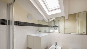 Une salle de bain moderne dotée d’un puits de lumière, d’une douche, d’un lavabo, d’un bidet et de toilettes.