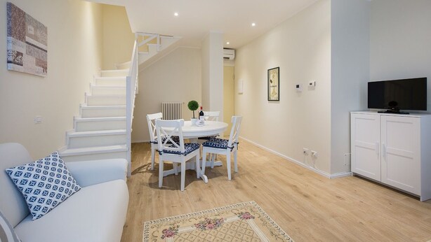 Un salon moderne avec un escalier, un coin repas et un meuble pour la télévision.