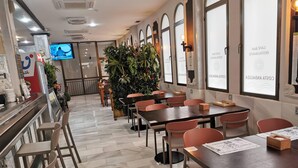A restaurant with marble flooring, red chairs, and tables. There are potted plants and a TV screen in the background. - Hotel Costa Andaluza (Motril)