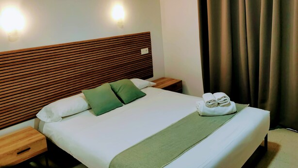 A neatly made bed with a wooden headboard, two pillows, a green throw blanket, and a set of towels on the side. - Hotel Costa Andaluza (Motril)
