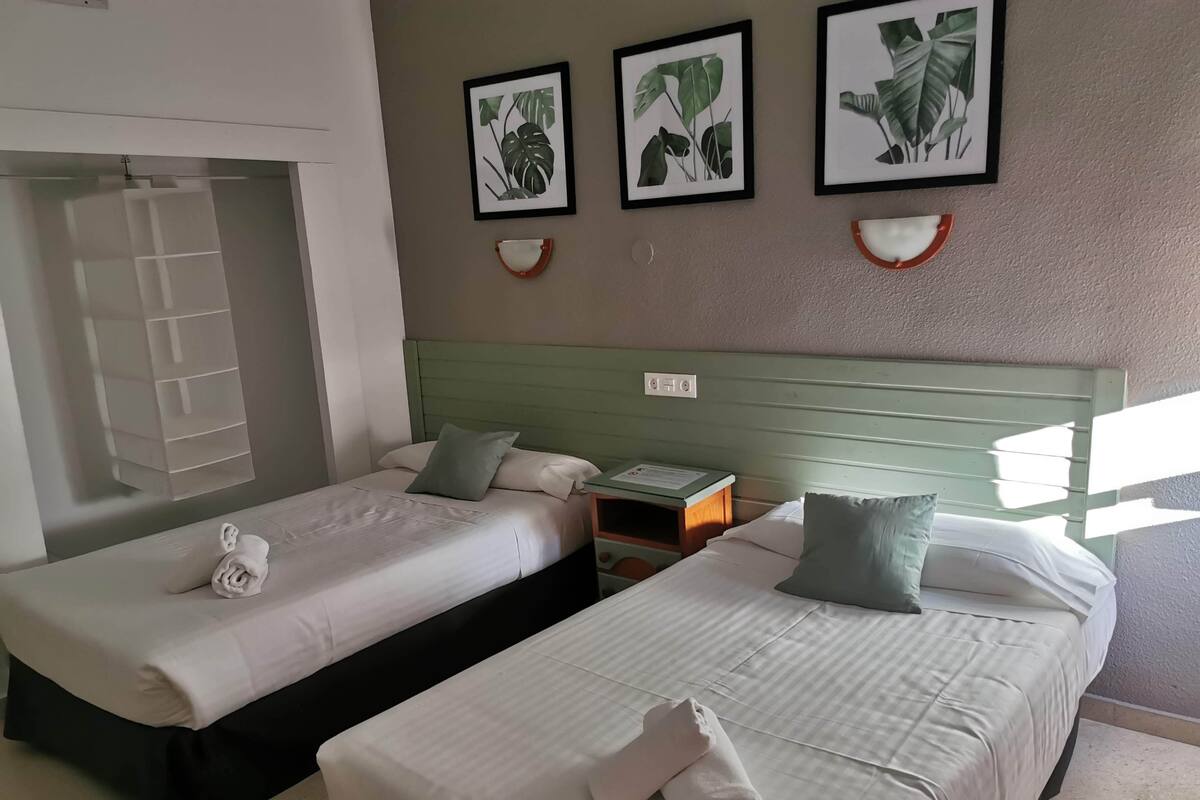 Ein Hotelzimmer mit zwei Betten, einem Nachttisch und gerahmten Pflanzenbildern an der Wand.